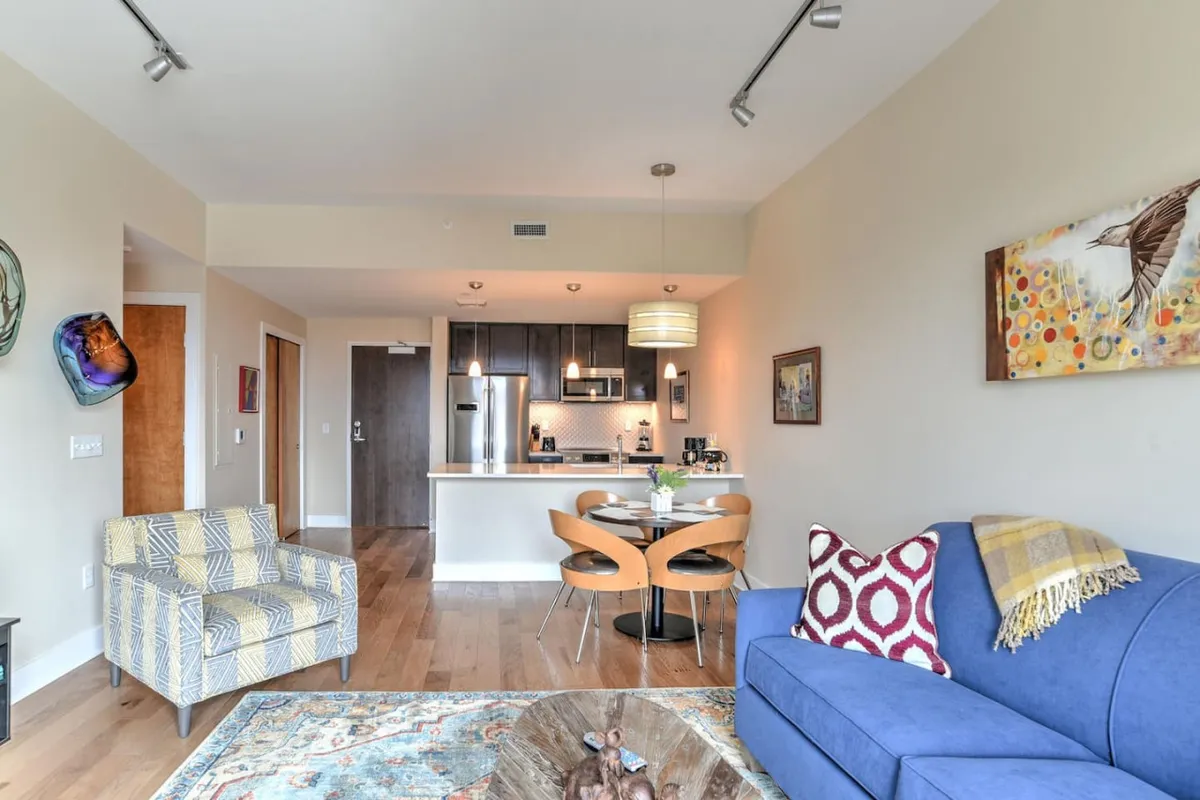 A spacious, open-plan interior with a blue sofa, dining table, textured rug, and art-adorned walls. The scene is perfect for entertaining or relaxing, supporting both human and pet-friendly comfort.