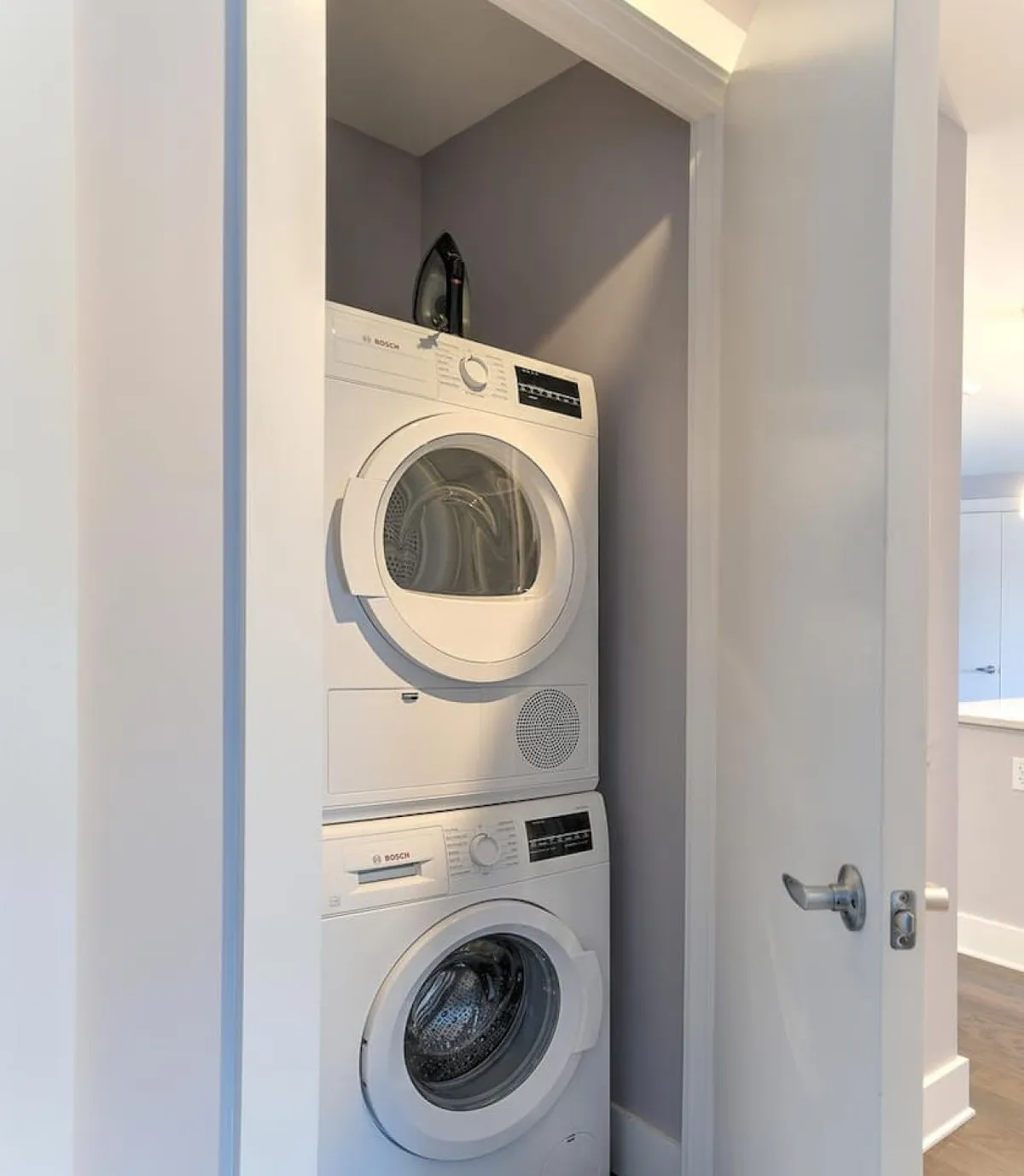 A compact, efficient laundry area featuring a stacked washer and dryer, with an iron placed on top. The scene is clean, organized, and functional, emphasizing practicality and ease for busy guests.